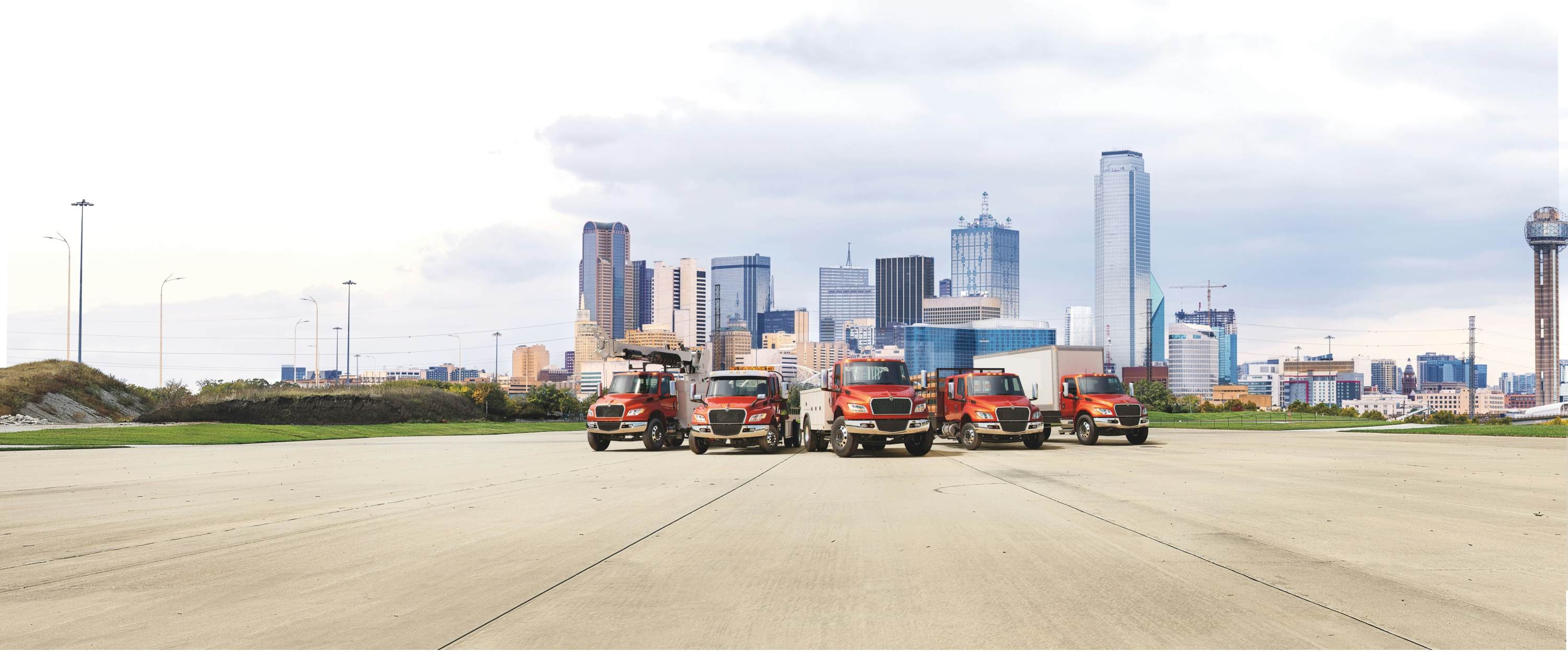 Five red MV Series Commercial Trucks parked in a row in front of a city landscape
