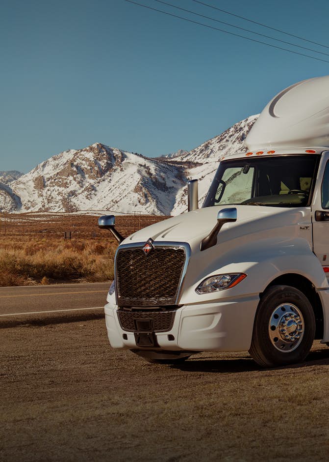 White truck driving along a road with snowy mountains in background