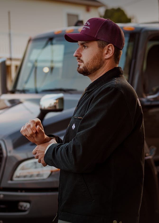Man in maroon baseball cap walking in front of grey truck