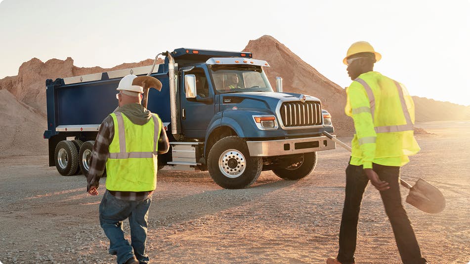 Two workers carrying equipment in front of a blue truck